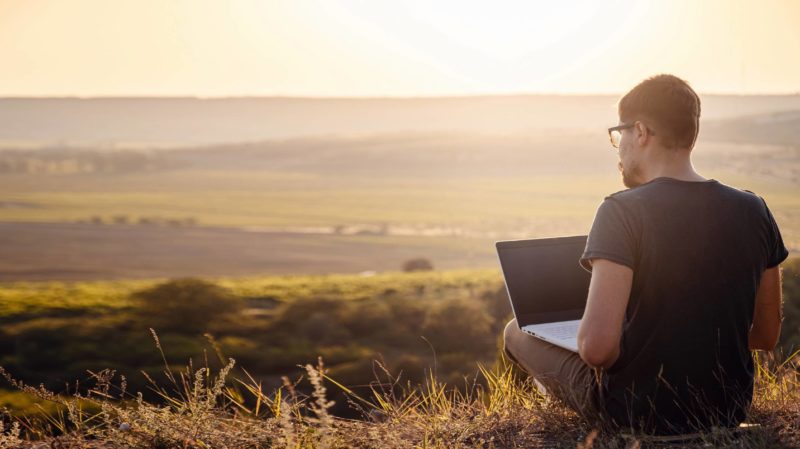 Man Overlooking a Landscape While Working on His Laptop