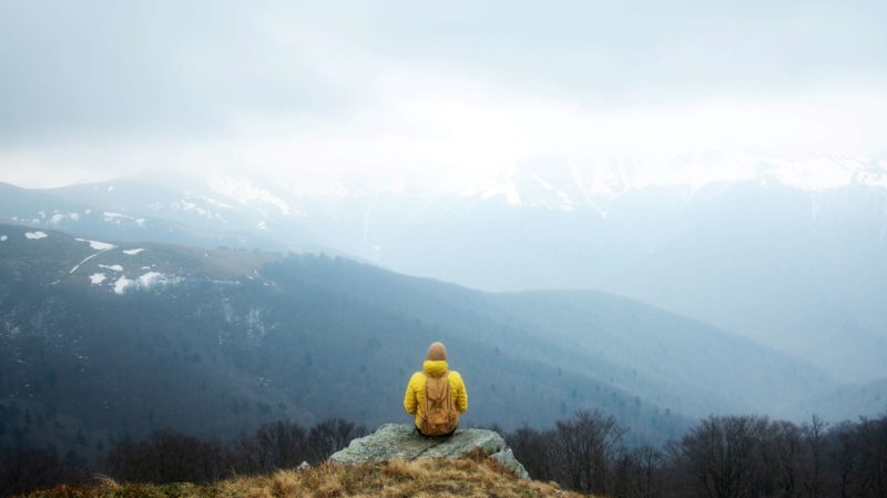 Person sitting on a rock looking out at mountain tops